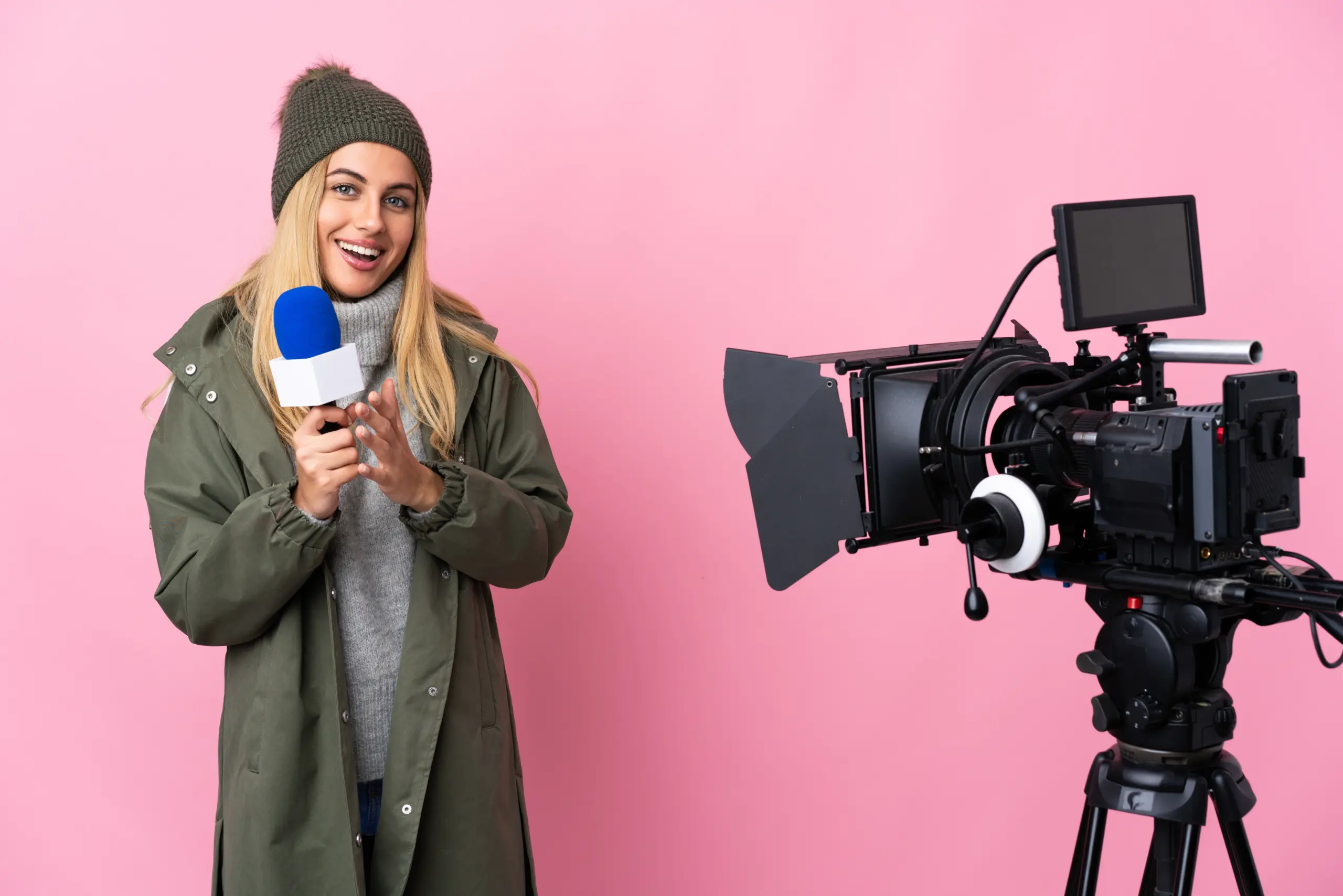 Reporter woman holding a microphone and reporting news over isolated pink background applauding