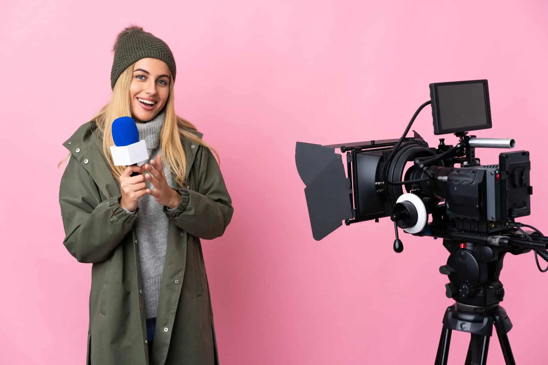 Reporter woman holding a microphone and reporting news over isolated pink background applauding
