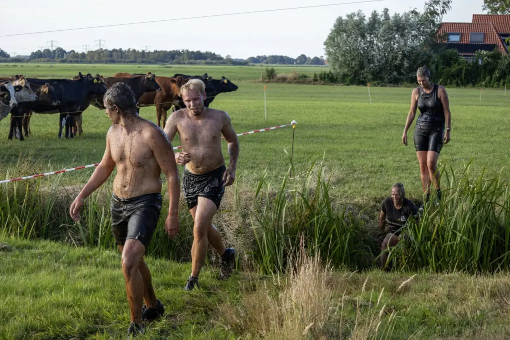 Vier deelnemers aan de Baggerrace lopen door het weiland, een van hen staat op het punt de sloot in te gaan.